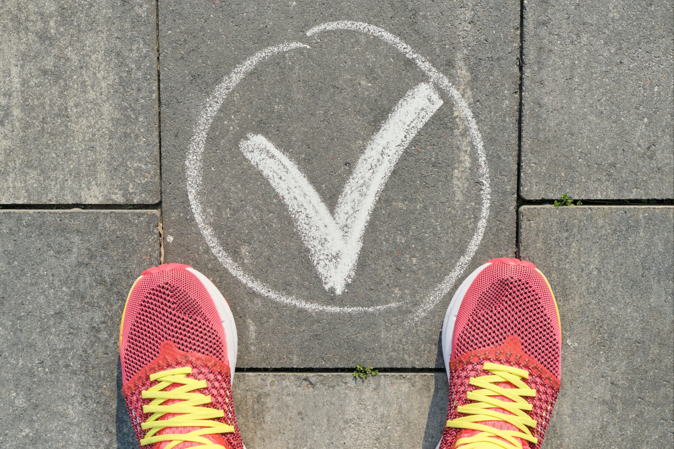 Checkmark ok sign on gray sidewalk with woman legs in sneakers, top view